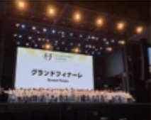 大きなステージに合唱団が並んで歌っている様子。